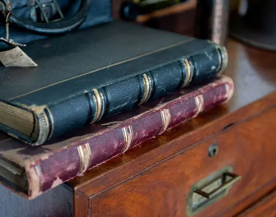 Two old books stack on each other on top of a wooden cabinet