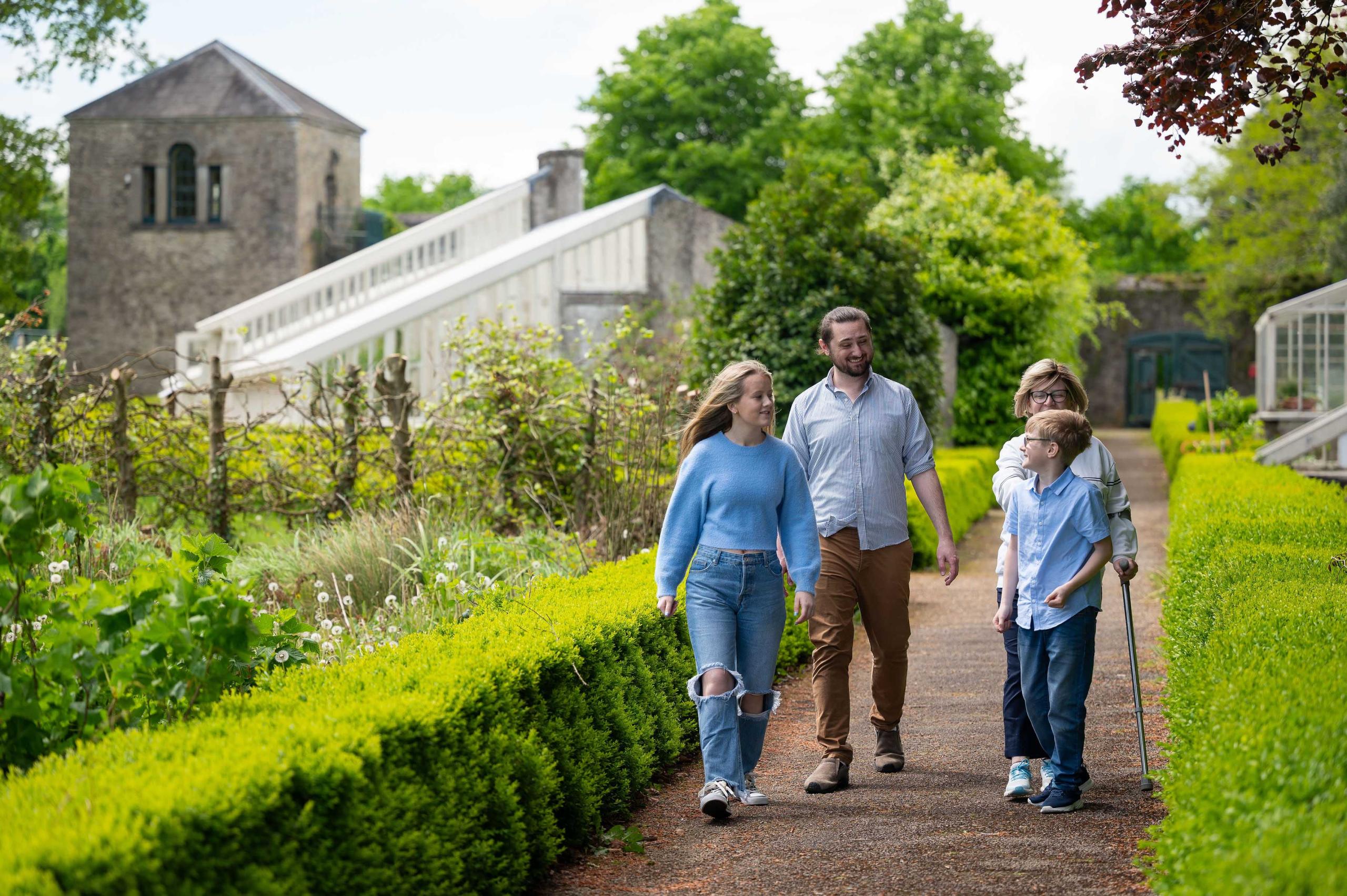 A family of four people walking in gardens with gazebo tower and historic glasshouse in background