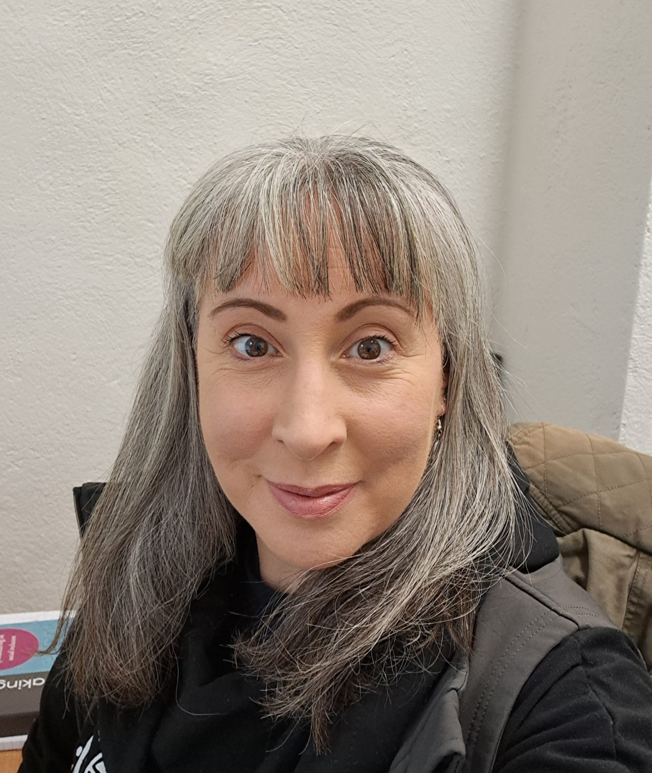 A head shot of a woman with grey hair smiling and wearing a grey/black jacket
