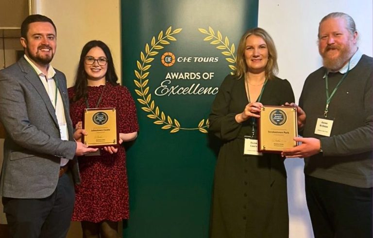 Two men and two women stand holding plaques in front of a sign which say CIE Tours Awards of Excellence