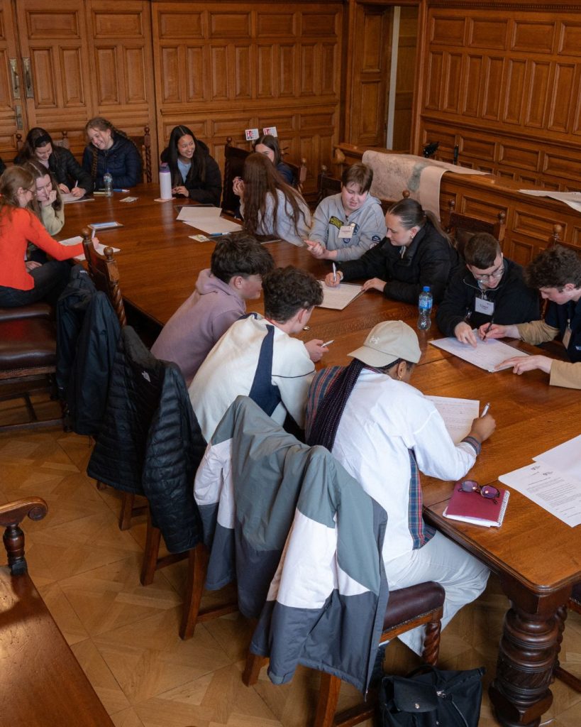 Transition year aged students sitting at a large wooden table with paper in front of them