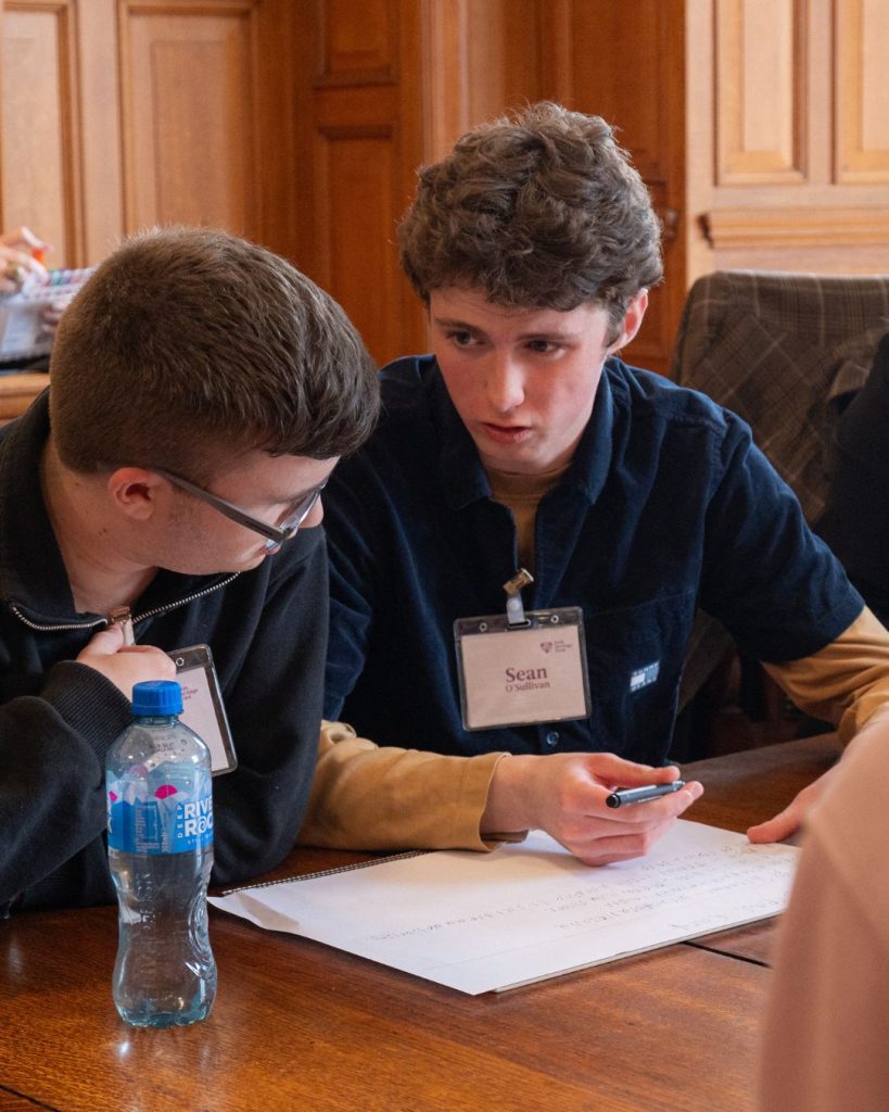 two transition year aged students concentrating, sitting at a large wooden table with paper in front of them
