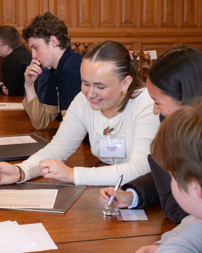 two transition year aged students smiling sitting at a large wooden table with paper in front of them