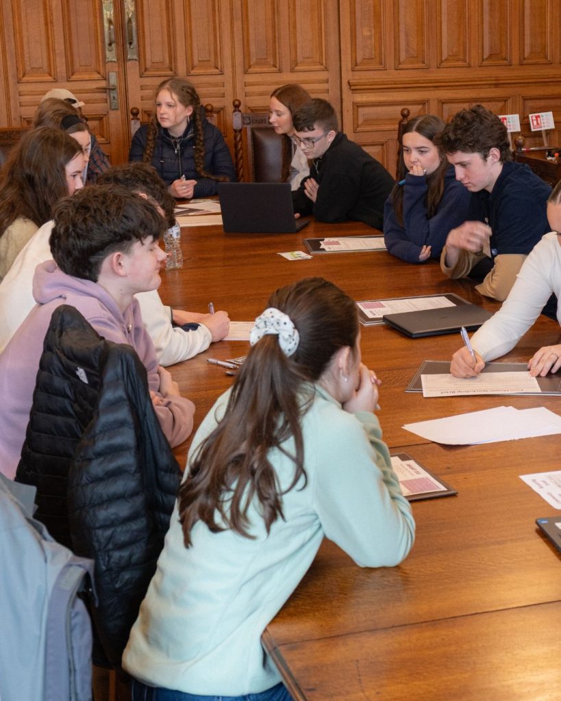 Transition year aged students sitting at a large wooden table with paper in front of them