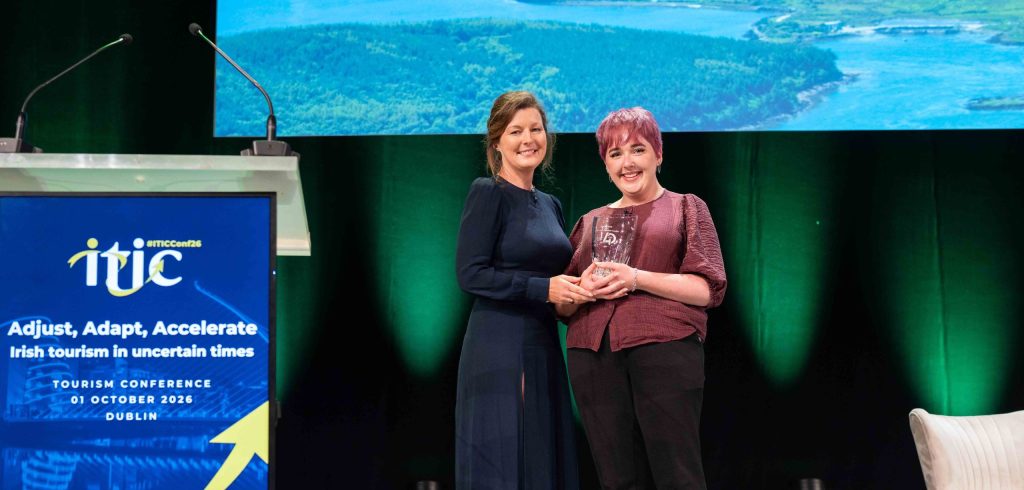 Two women stand on stage, one with an award in her hands. In the foreground is a lectern with the logo of ITIC.