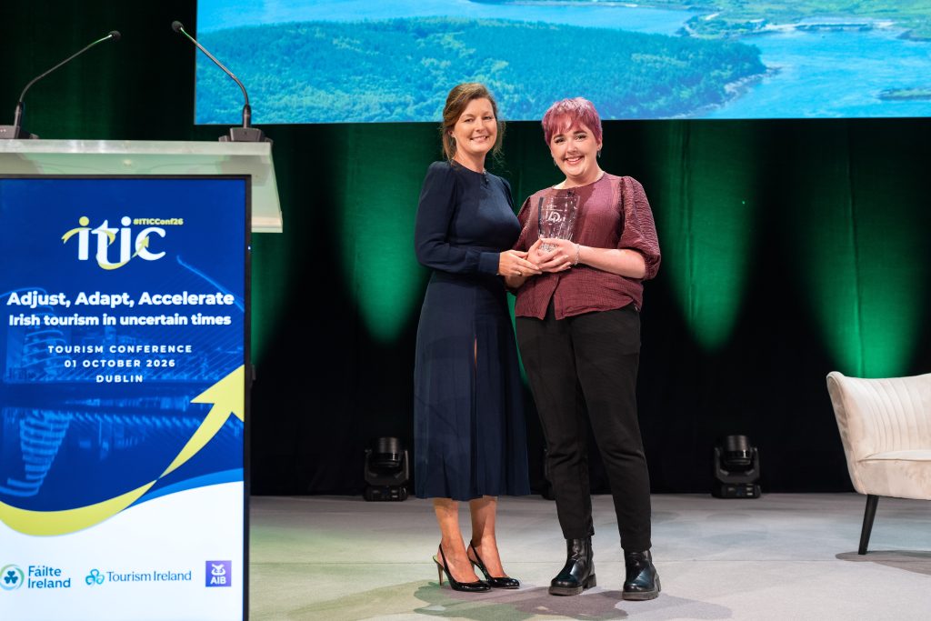 Two women stand on stage, one with an award in her hands. In the foreground is a lectern with the logo of ITIC.